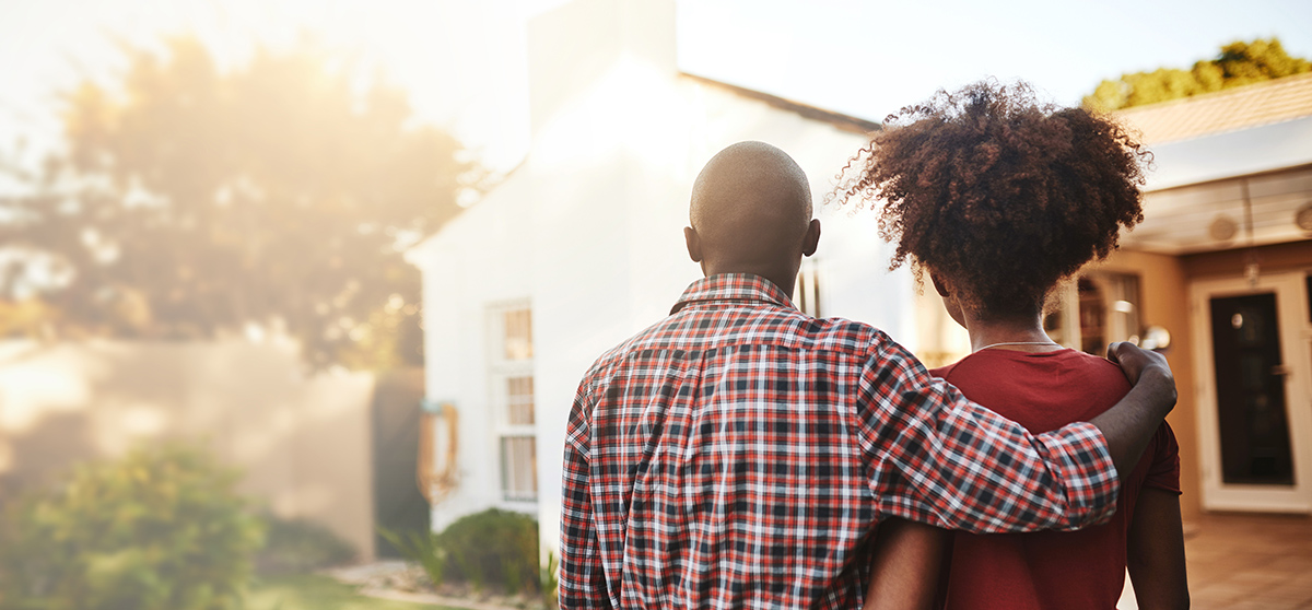 Young couple with arms around each other looks at their new home